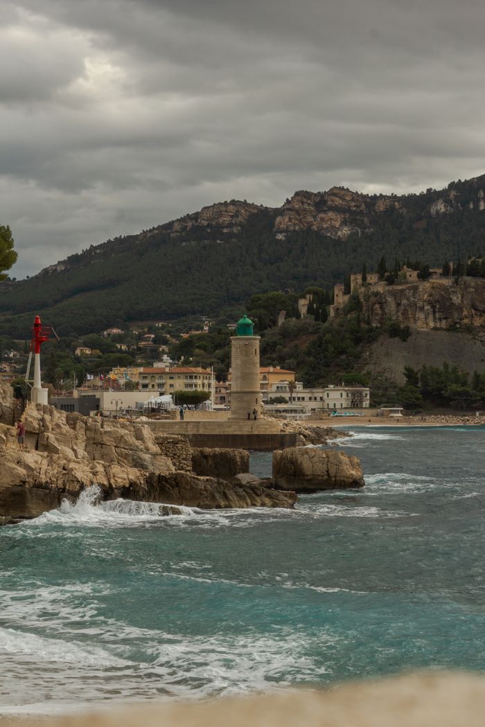 services-01 Beautiful coastal landscape of Cassis, France with a lighthouse and rocky shore against a mountainous backdrop.