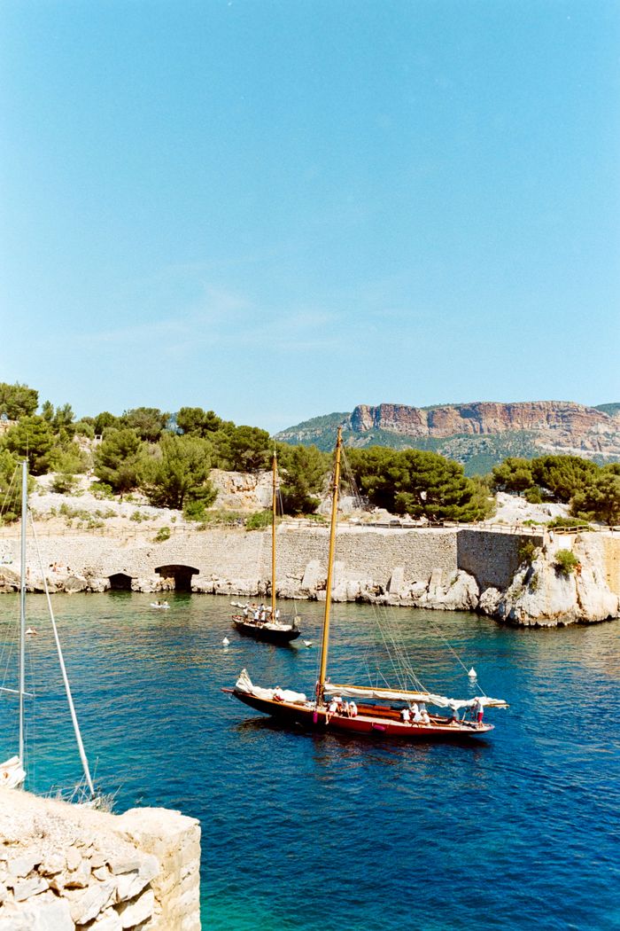 Sailboats cruising in the vibrant waters of Cassis harbor under a clear blue sky.